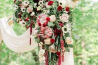 a refined and chic wedding arch with white fabric, blush and burgundy roses, carnations, white anemones, greenery and amaranthus
