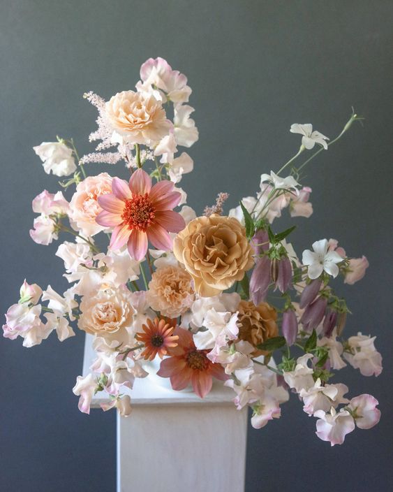 a refined and delicate wedding centerpiece of neutral sweet peas and pink and rust blooms is a lovely idea for spring