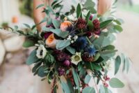 a refined fall wedding bouquet of blush peony roses, burgundy blooms, blue thistles, greenery and amaranthus is wow
