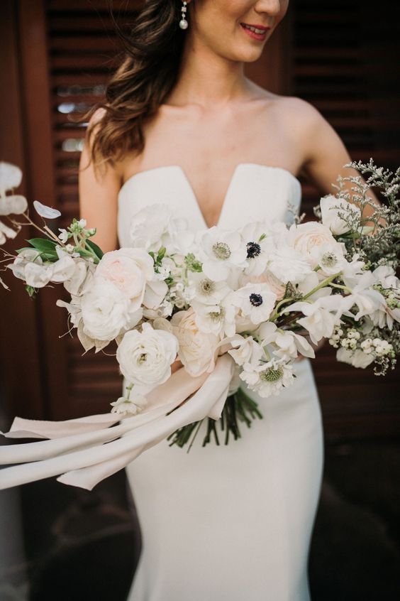 a refined wedding bouquet of blush and white ranunculus, anemones, lunaria and greenery is a stunning idea for a spring or summer wedding