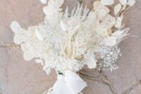 a refined white wedding bouquet of dried leaves, bunny tails, baby’s breath and lunaria and white ribbon is super chic