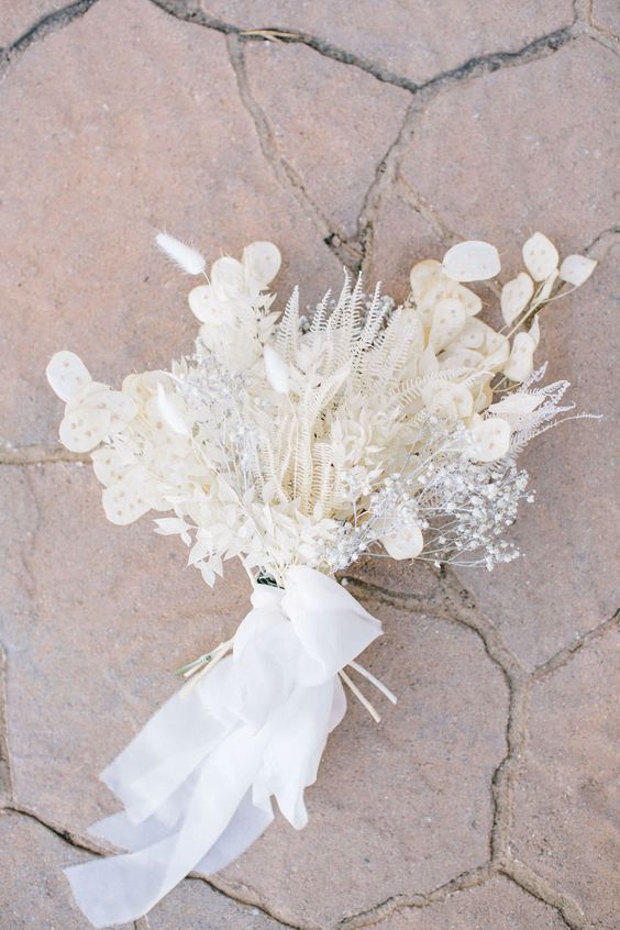 a refined white wedding bouquet of dried leaves, bunny tails, baby's breath and lunaria and white ribbon is super chic