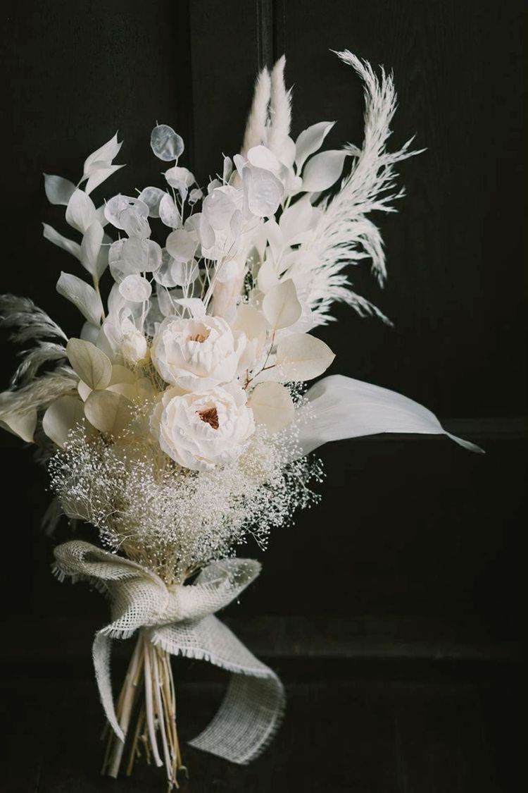 a refined white wedding bouquet of ponies, lunaria, dried leaves and grasses, some baby's breath and a white burlap wrap