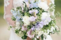 a romantic wedding bouquet of lilac sweet peas, blue deliphinium, white and lilac roses and greenery for a spring or summer wedding