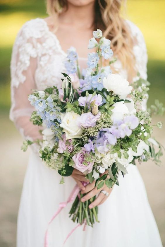 a romantic wedding bouquet of lilac sweet peas, blue deliphinium, white and lilac roses and greenery for a spring or summer wedding