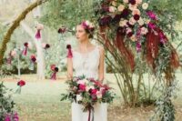 a round wedding arch decorated with moss, greenery and bold purple, burgundy, pink and deep red blooms and foliage