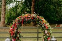 a rounded wedding arch covered with greenery, blush, white, red, fuchsia, yellow, orange dahlias and roses and amaranthus