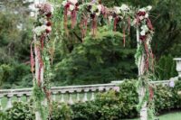 a rustic wedding arch covered with greenery, white and burgundy blooms and amaranthus and moss is a cool idea for a rustic or woodland wedding