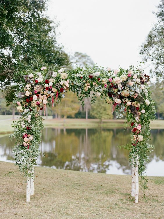 a rustic wedding arch done with greenery, blush, white and burgundy roses and dahlias, hydrangeas and amaranthus