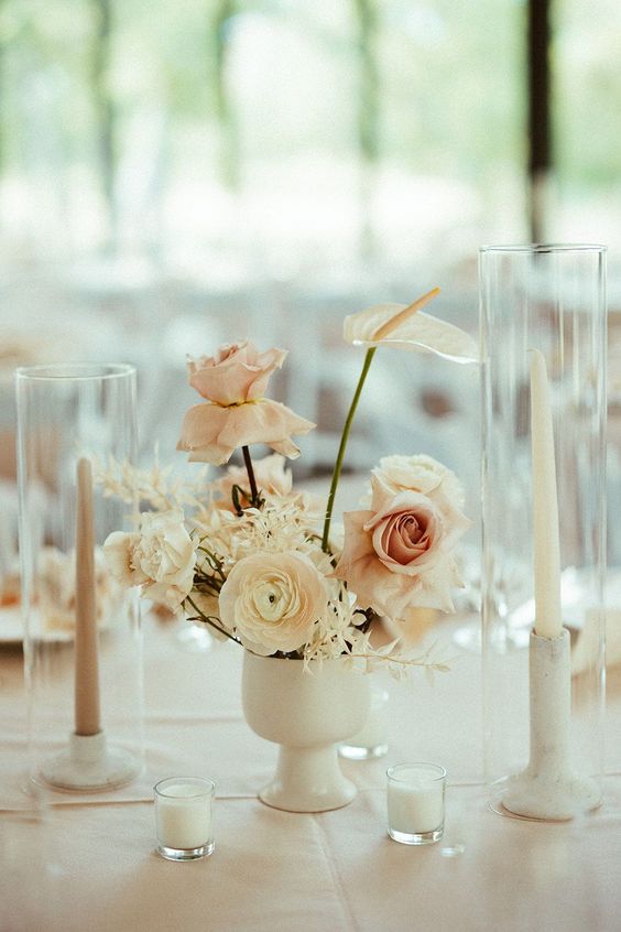 a small and cool wedding centerpiece of white ranunculus, anthuriums, blush roses and candles around is wow