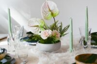 a small wedding centerpiece of fern, blush carnations and white anthuriums plus green candles around is wow