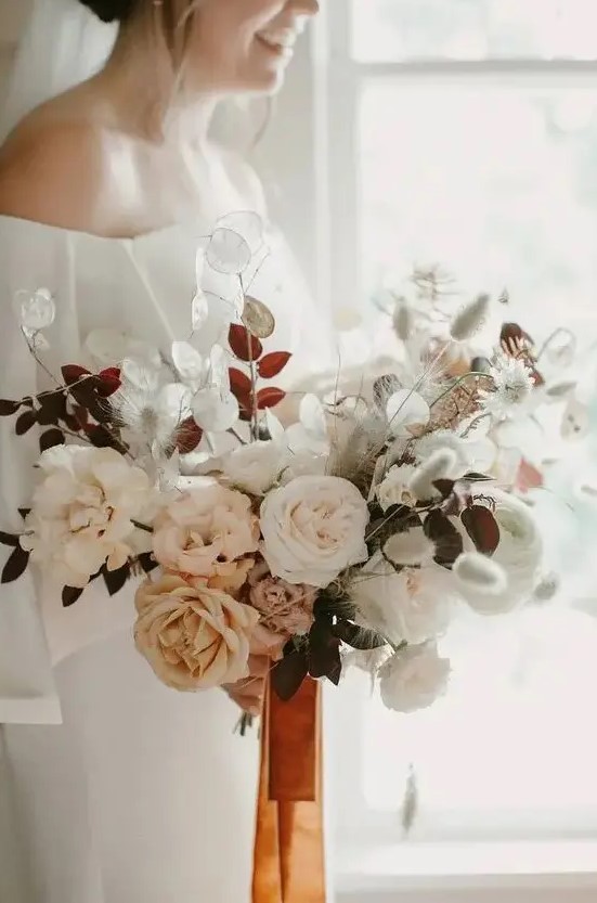 a soft pastel wedding bouquet with white and blush blooms plus herbs and orange ribbons for a delicate look