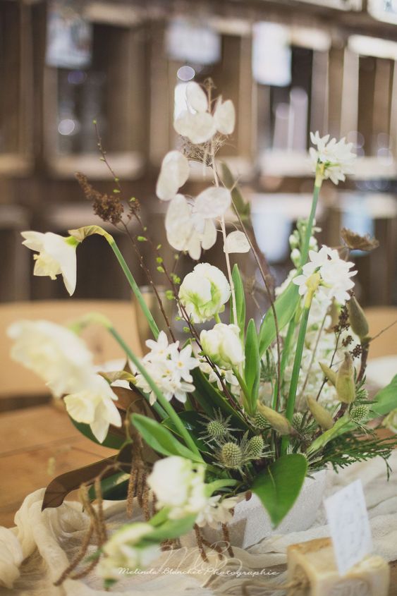 a spring wedding centerpiece of daffodils, lunaria, thistles, greenery and some twigs is a relaxed and cool idea