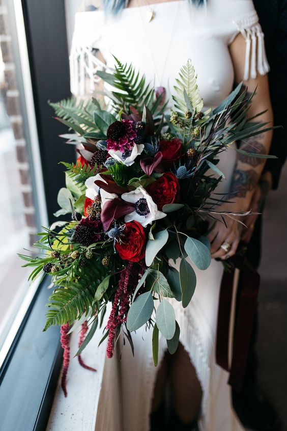 a statement boho wedding bouquet of red roses, white anemones, greenery, thistles, berries and amaranthus is super cool