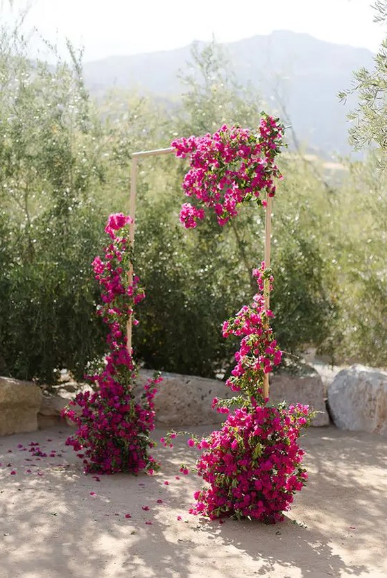 a stylish modern wedding arch decorated with bougainvillea and greenery is a cool idea for a summer or fall wedding