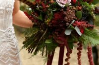 a sumptuous fall wedding bouquet of pink and burgundy roses, deep purple callas, berries, feathers and amaranthus plus some greenery