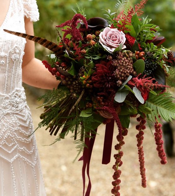 a sumptuous fall wedding bouquet of pink and burgundy roses, deep purple callas, berries, feathers and amaranthus plus some greenery