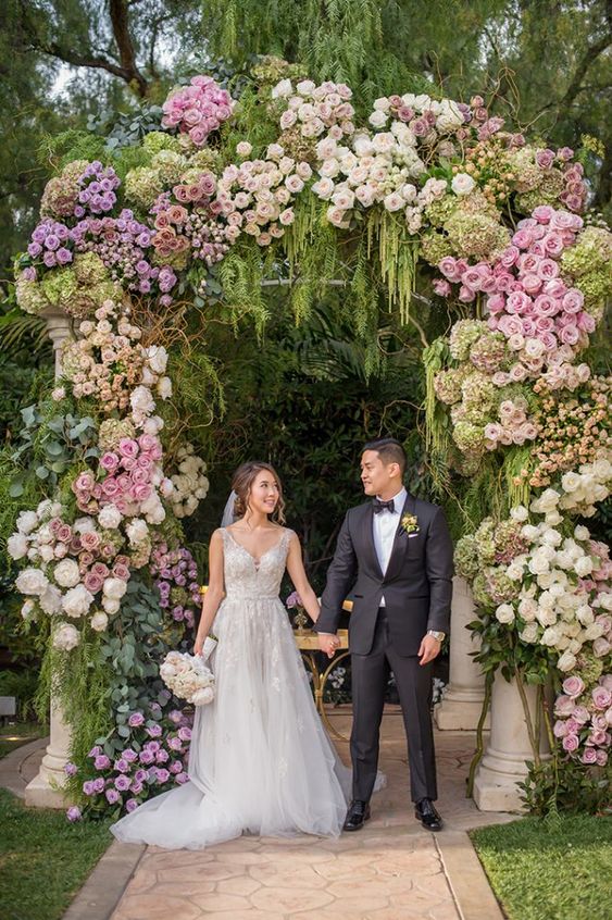 a super lush wedding arch with greenery, green amaranthus, blush, white, lilac, pink roses and peonies for a garden wedding