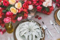 a super lush wedding centerpiece of bougainvillea, yellow and blush roses, red ones, candles and air plants on each palce setting