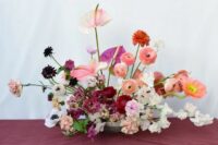 a super lush wedding centerpiece of pink ranunculus, carnations and roses, deep purple blooms and anthuriums