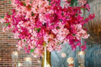 a tall and bold wedding centerpiece of a gold vase and bougainvillea and tall candles plus a matching table runner are a cool combo