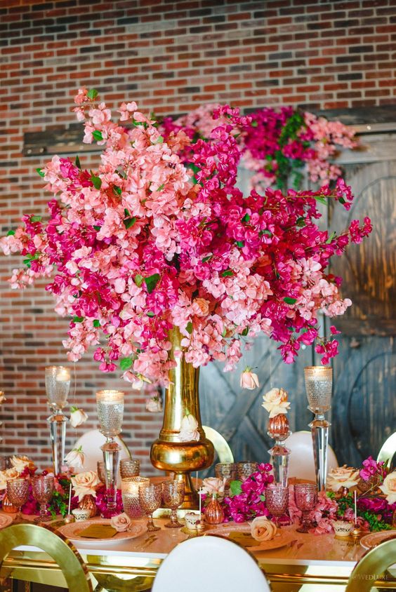 a tall and bold wedding centerpiece of a gold vase and bougainvillea and tall candles plus a matching table runner are a cool combo