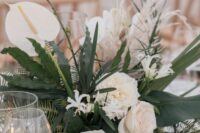 a textural wedding centerpiece of greenery and ferns, white roses, anthruiums and grasses is amazing for a tropical wedding