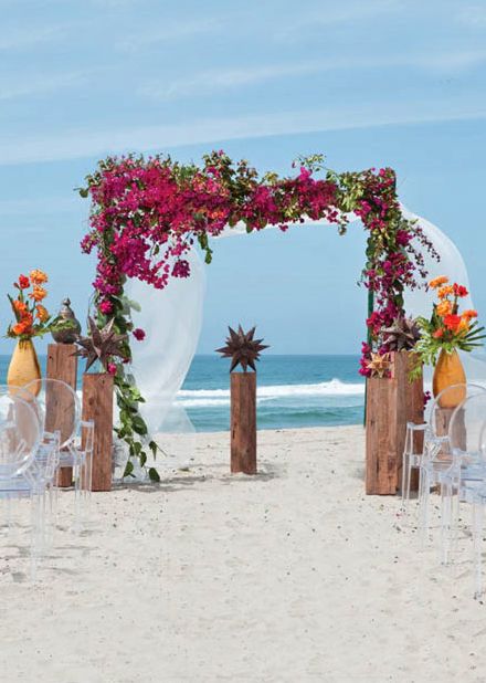 a tropical wedding arch covered with bougainvillea, greenery and bold tropical blooms and greenery for a beach wedding