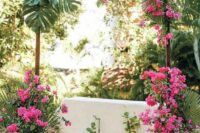 a tropical wedding arch covered with fronds and with bougainvillea, mostly in pots to make it more eco-friendly