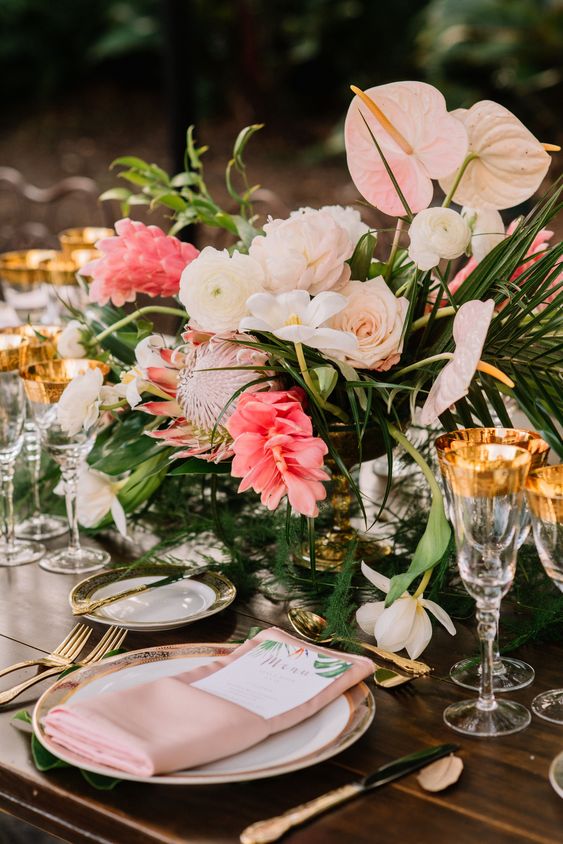 a tropical wedding centerpiece of blush roses, anthuriums, ranunculus, coral tropical blooms and greenery is amazing