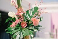 a tropical wedding centerpiece of pink anthuriums, blooming branches and fronds and leaves is a cool and stylish idea