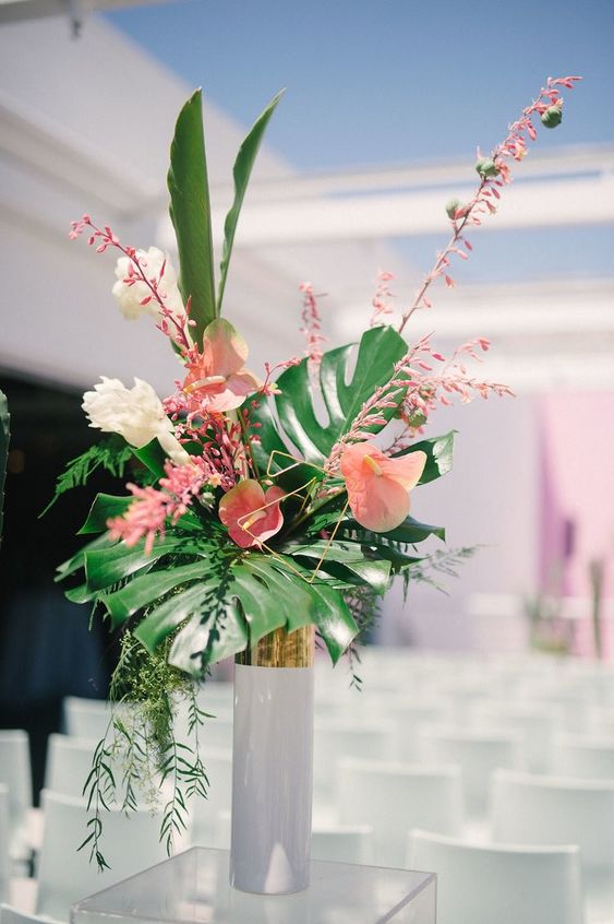 a tropical wedding centerpiece of pink anthuriums, blooming branches and fronds and leaves is a cool and stylish idea