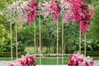 a vibrant modern wedding arch covered with white, light pink and fuchsia blooms including bougainvillea and matching arrangements lining up the aisle