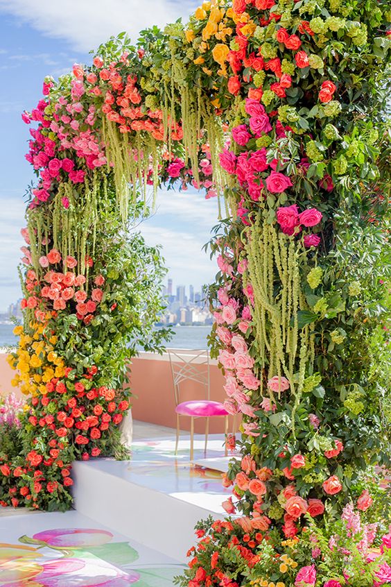a vibrant wedding arch of greenery, green amaranthus, pink, red, light pink, yellow roses and garden roses for a wow factor