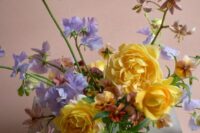 a vibrant wedding centerpiece of yellow roses, lilac sweet peas and greenery is a cool idea for a bold spring or summer wedding