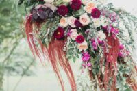 a wedding arch decorated with a bold arrangement of blush and burgundy blooms, dark foliage, greenery and amaranthus