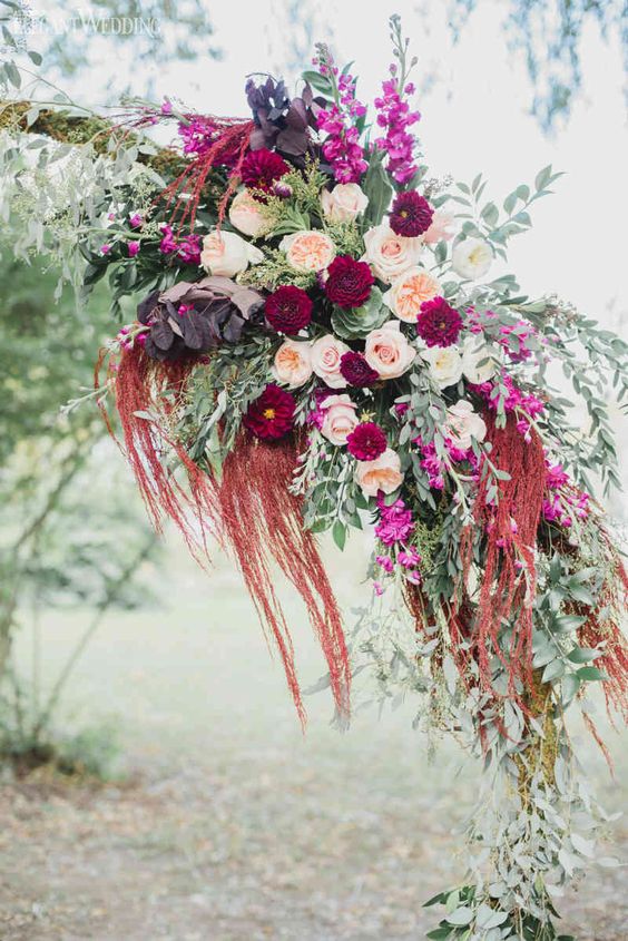 a wedding arch decorated with a bold arrangement of blush and burgundy blooms, dark foliage, greenery and amaranthus
