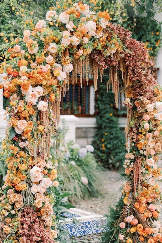 An adorable wedding arch covered with blush, coffee colored, rust and marigold blooms, a bit of greenery and amaranthus