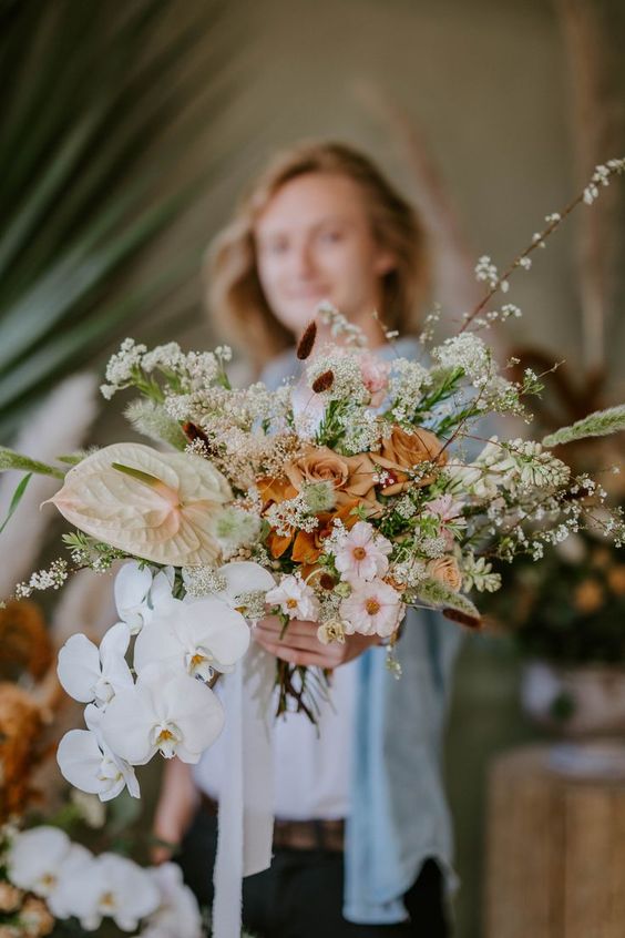 an airy wedding bouquet of rust roses, neutral daisies and orchids plus anthurium and blooming branches