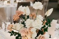 an exquisite wedding centerpiece of blush and white roses, greenery and anthuriums plus candles around is amazing
