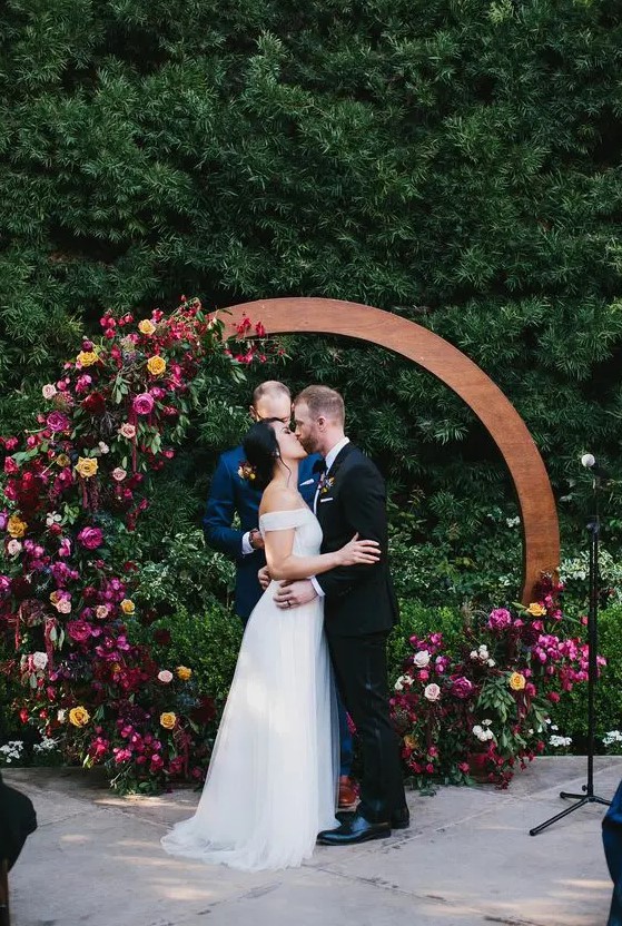 an extra bold jewel tone round wedding arch done with burgundy, deep purple, fuchsia, yellow blooms and greenery