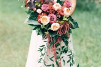 an eye-catching wedding bouquet of burgundy roses, blush peony roses, greenery, dark foliage, amaranthus, some grasses