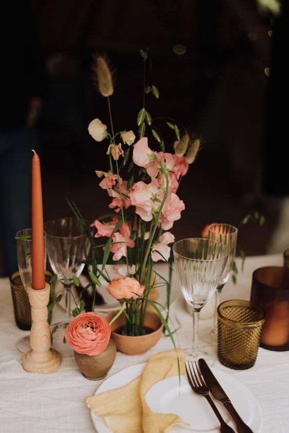 an ultra-modern wedding centerpiece of pink and peachy sweet peas and bunny tails ina  terracotta pot and some pink ranunculus