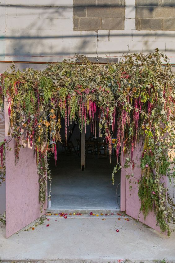 pink barn doors decorated with greenery and branches, yellow blooms and amaranthus are amazing as a wedding arch
