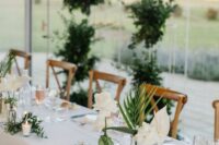 stylish modern wedding centerpieces of greenery and tropical leaves, white roses and anthuriums plus candles