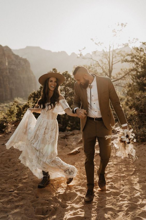 a boho groom outfit with a brown pantsuit, a white shirt with black buttons, brown shoes and a bolo tie
