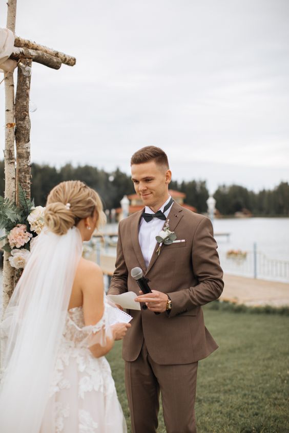 a brown pantsuit, a white shirt, a black bow tie and a boutonniere are a cool combo for a modern rustic groom's look