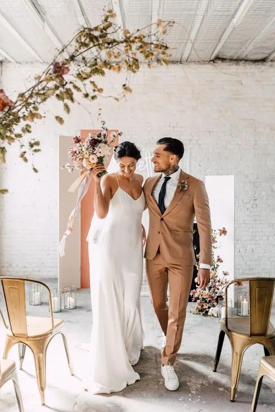 a lovely modern groom's look with a beige pantsuit, a white shirt, white sneakers and a black tie are a great combo