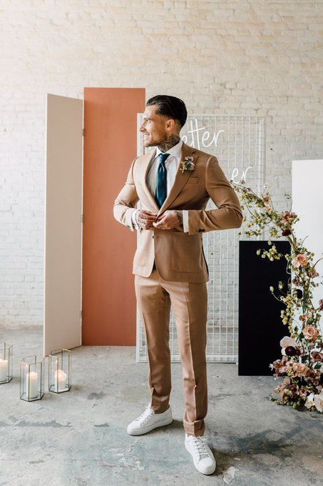 a modern groom's look with a beige pantsuit, a white shirt, a black tie and white sneakers is a super chic and cool idea