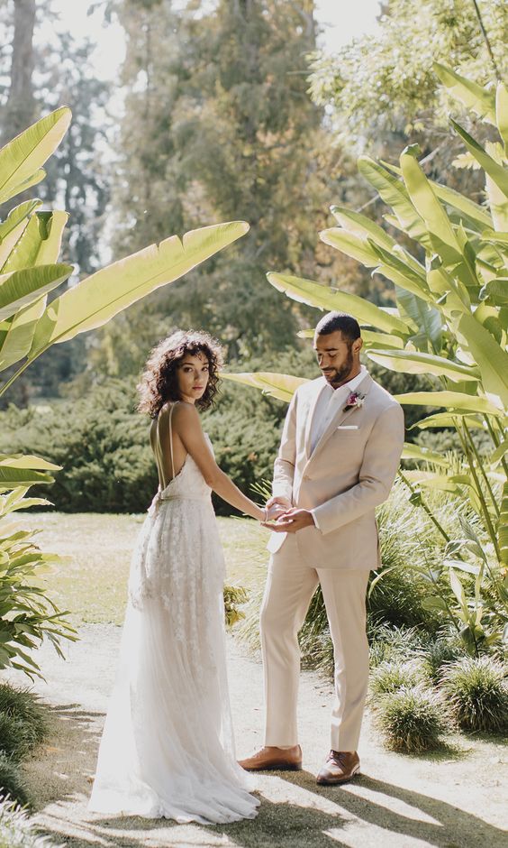 a modern tropical groom's outfit with a tan pantsuit, a white shirt, amber shoes and a bright boutonniere is super cool